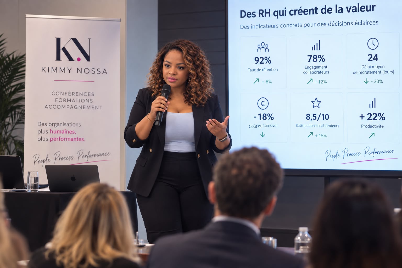 Kimmy Nossa en prise de parole lors d’une conférence RH, micro en main, devant un public et un écran de données RH.